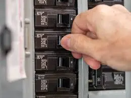 A hand flips a breaker on an electrical panel